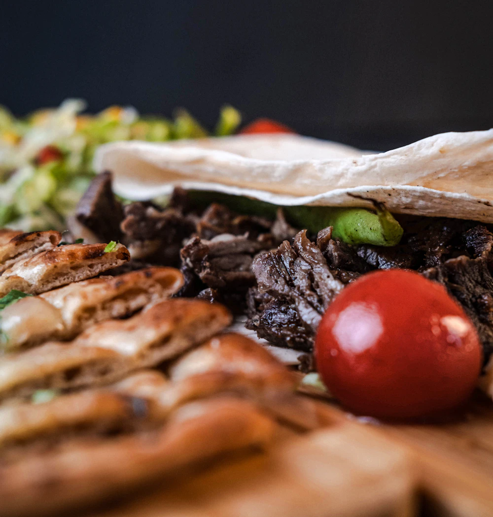 Pan de kebab relleno de carne asada con tomate, sobre una tabla de madera